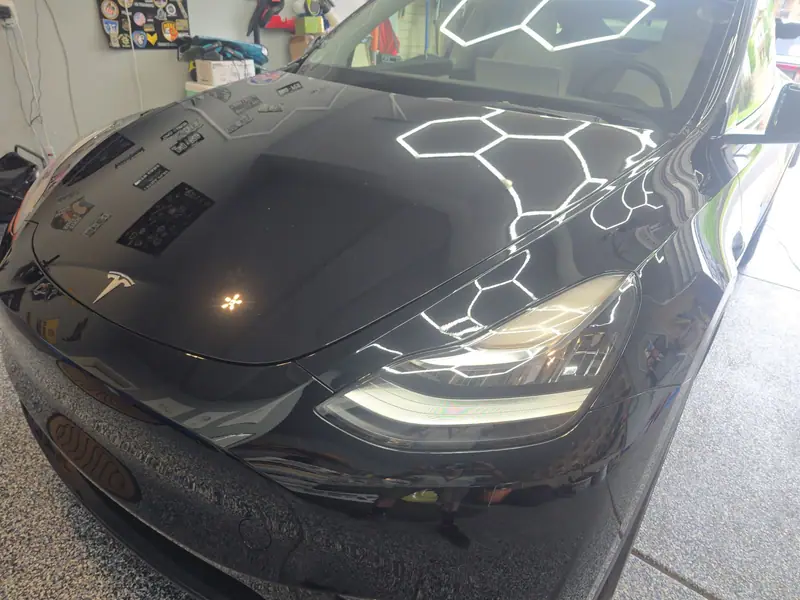 Black Tesla hood with a deep, clean reflection of hexagon lights after paint correction and coating
